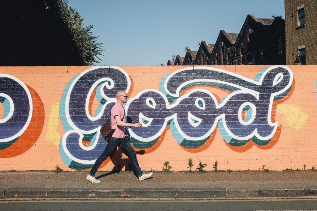 mann geht vor graffiti wand spazieren mit schriftzug good